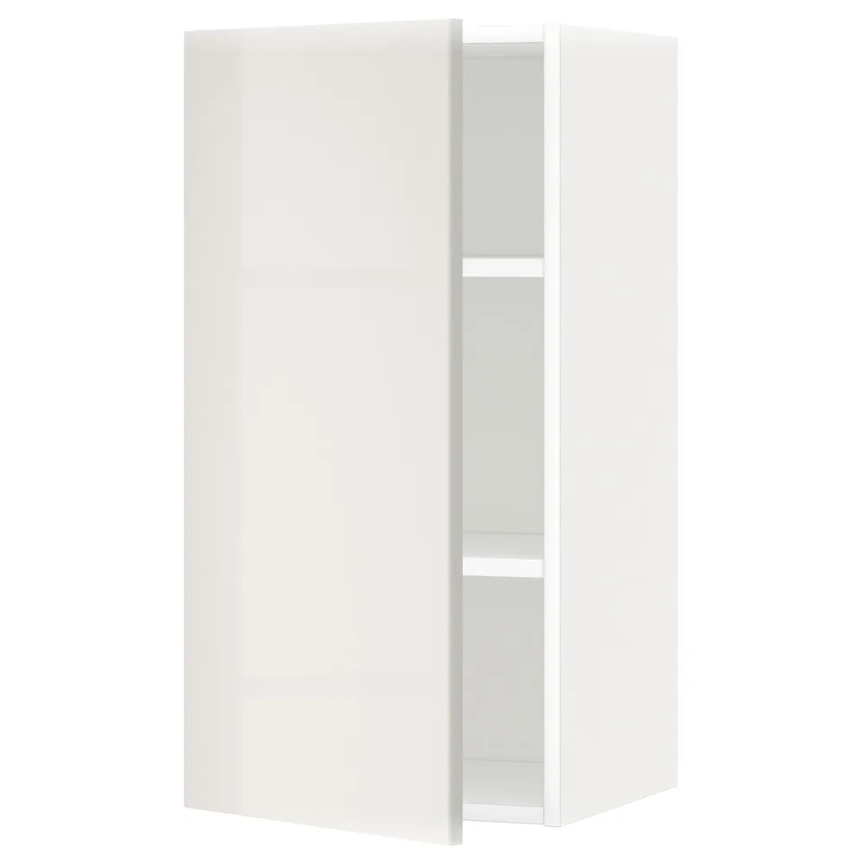 Depicts a white METOD wall cabinet from IKEA, featuring a high gloss finish, with one door slightly open, revealing an adjustable shelf inside.