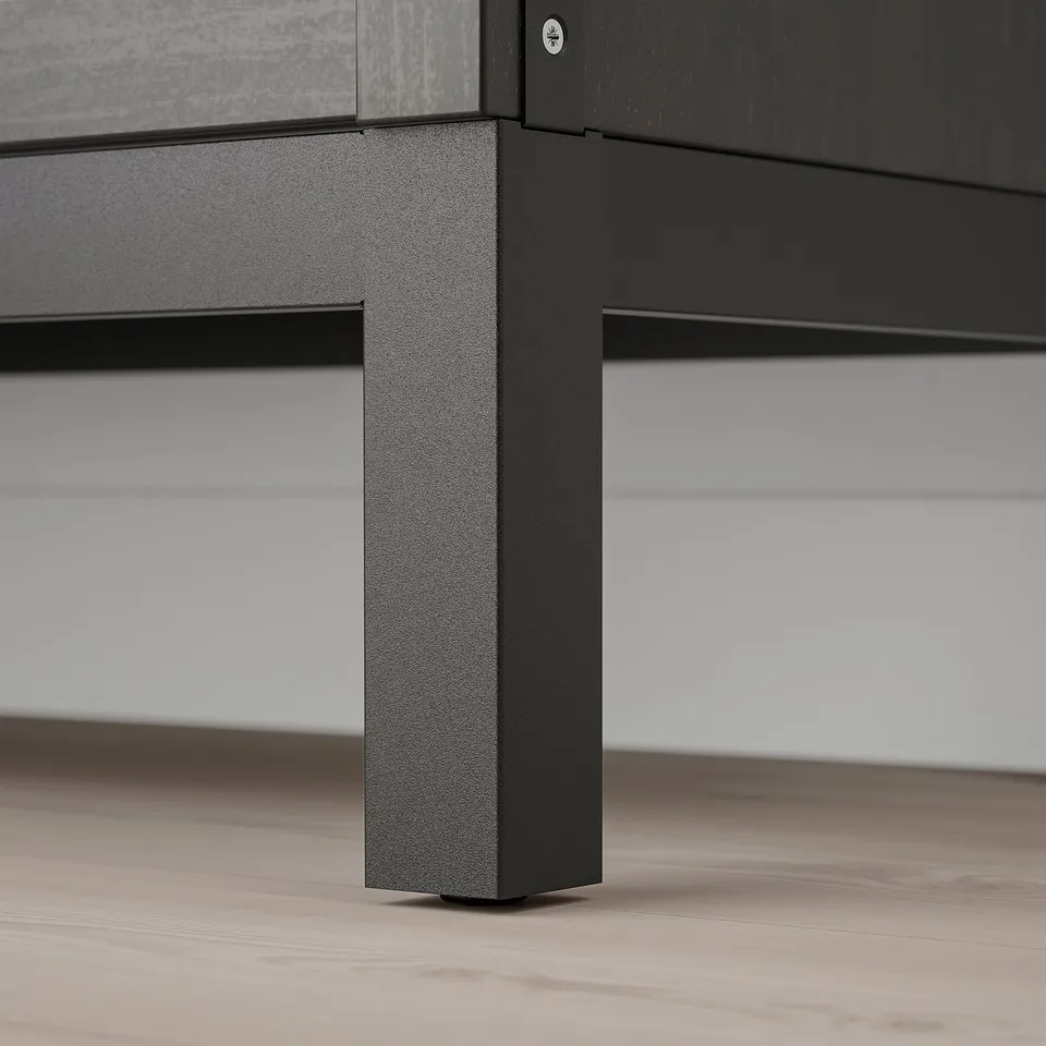 Black metal shelf leg with textured finish on wooden floor, supporting sleek, minimalist furniture.
