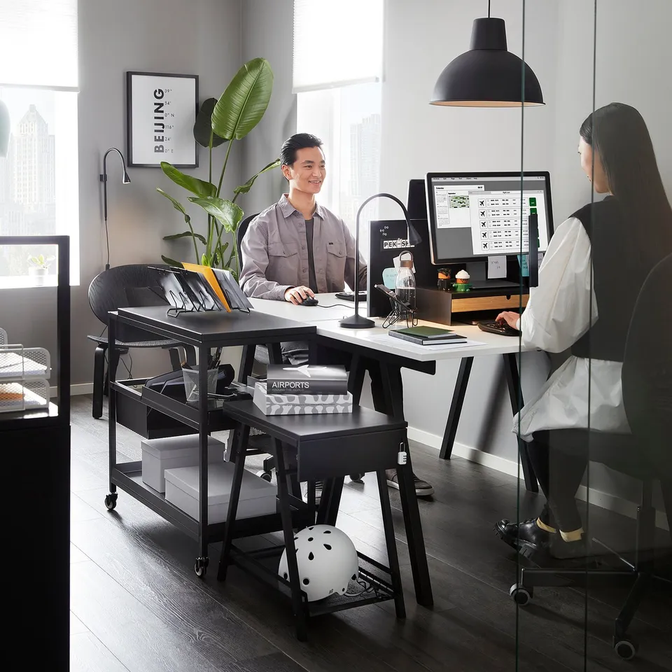 People working at desks with computers. Black TROTTEN storage under desk, lockable drawer, helmet shelf.
