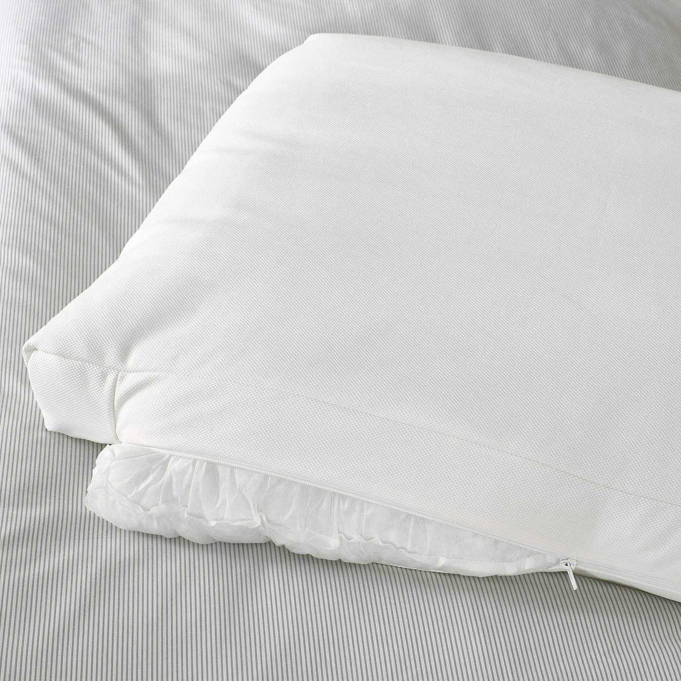 A large white rectangular pillow on a striped sheet, likely part of a bed frame with upholstered cushions and sloped headboard.