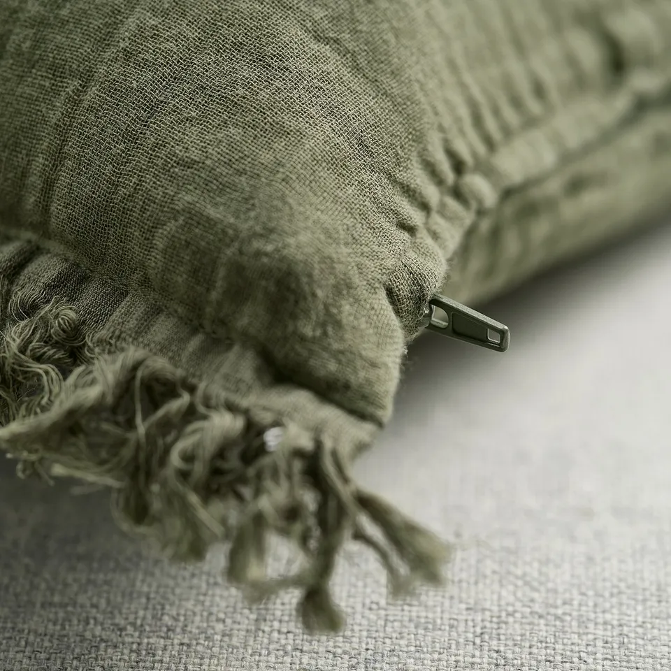 Folded green cushion cover with zip, soft cotton material, frayed edges.