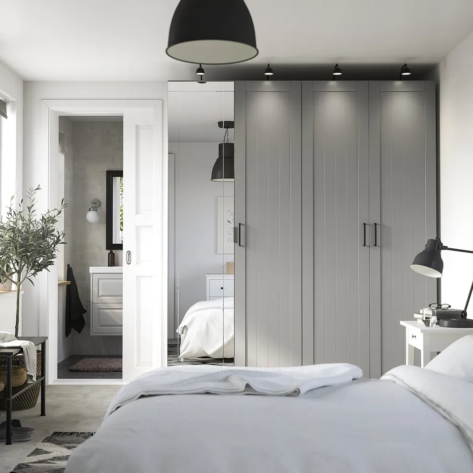 Modern bedroom with grey PAX wardrobe, mirrored door, white bed, and black accents.