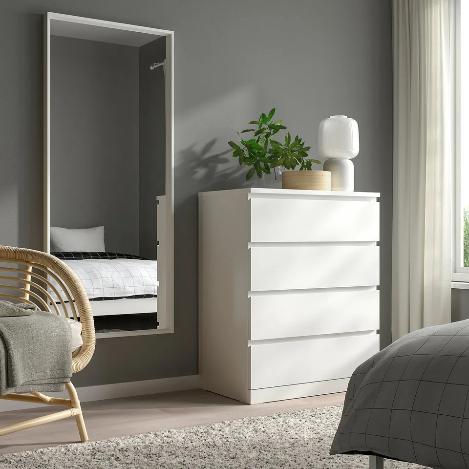 Modern bedroom with large white NISSEDAL mirror, wide drawers, and wicker chair against grey walls with beige curtains.