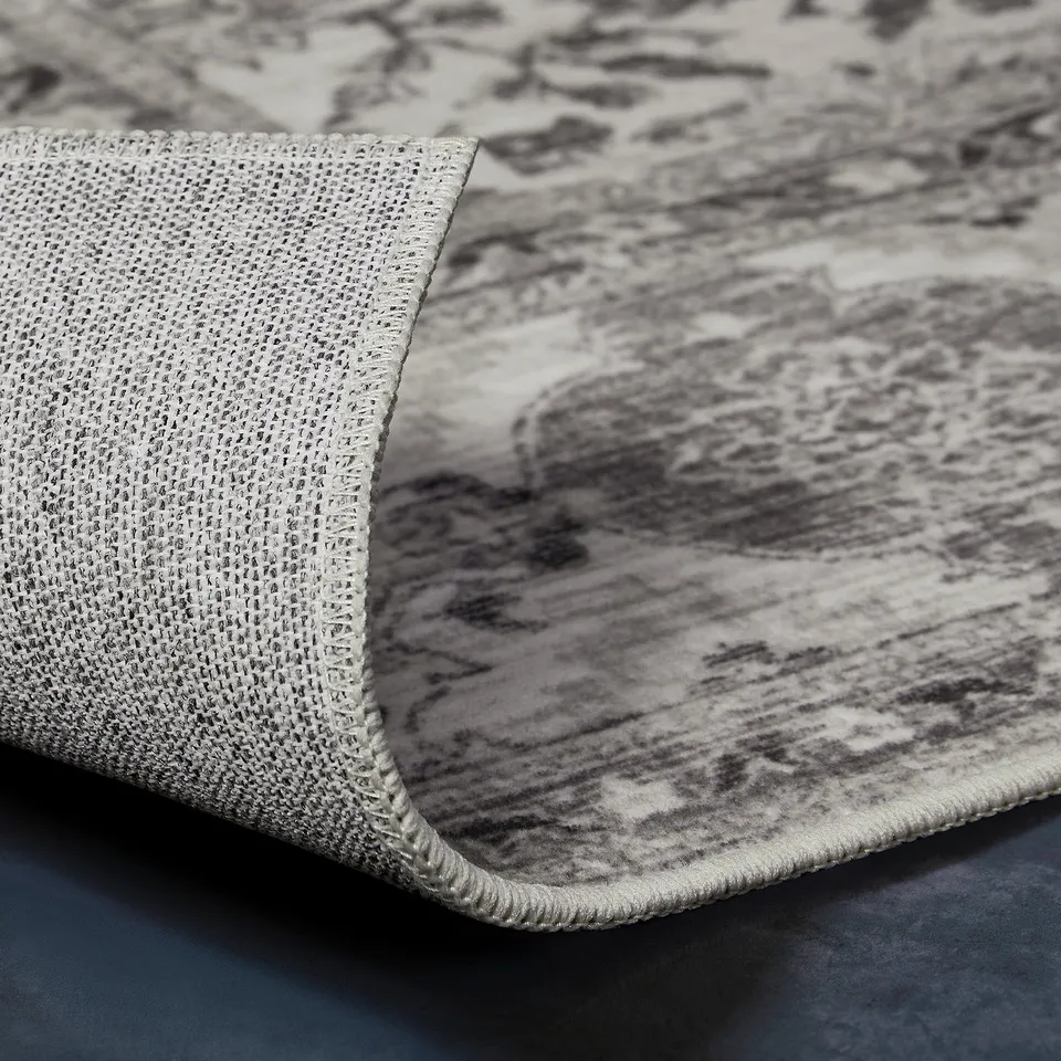 Close-up of a textured, grey, eco-friendly mat with a woven edge, featuring a recycled rubber middle and polyester surfaces.