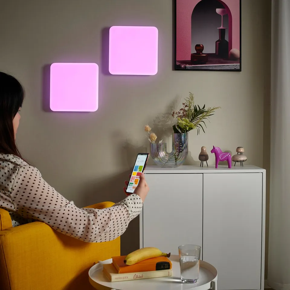 Person adjusts smart light panel colour using smartphone in living room.