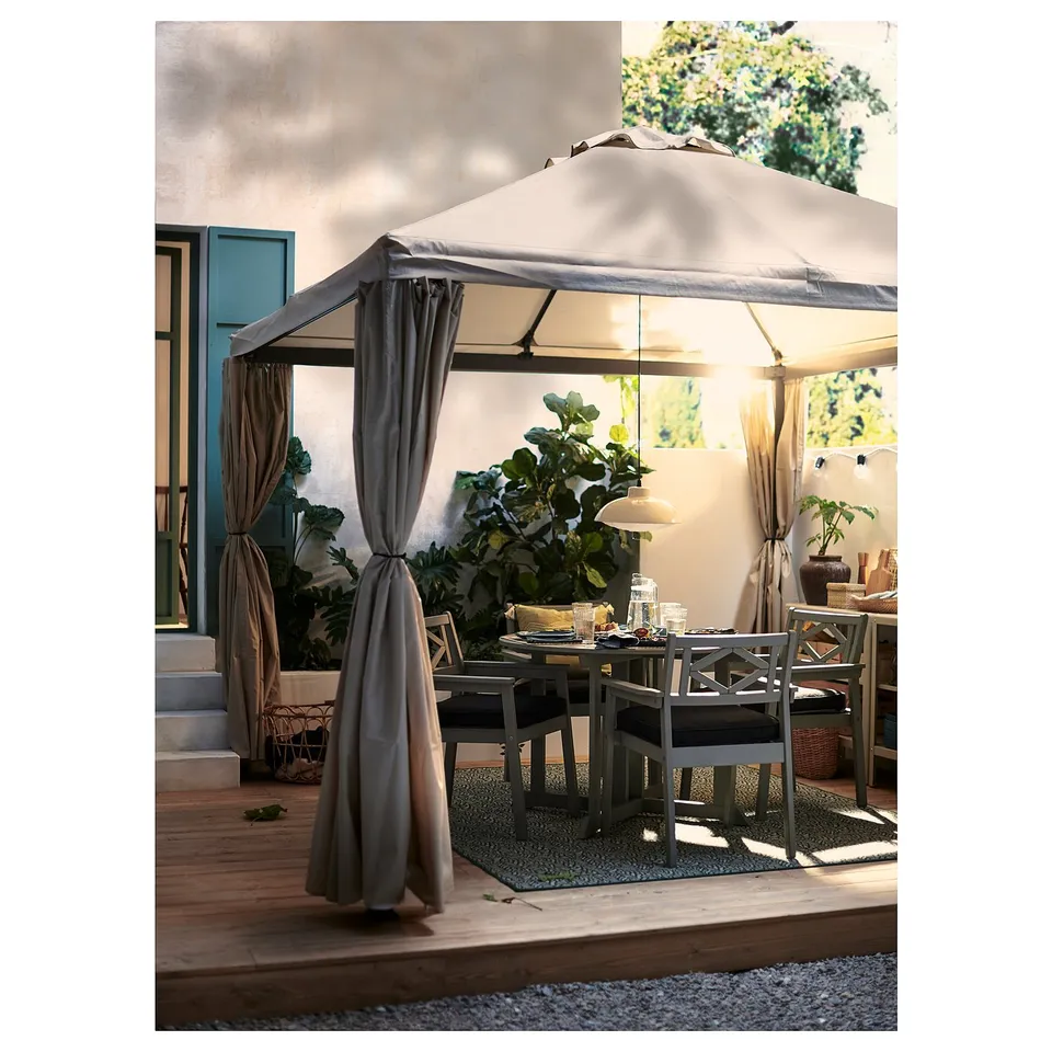 Outdoor dining area with grey canopy and curtains providing privacy, surrounded by lush greenery.