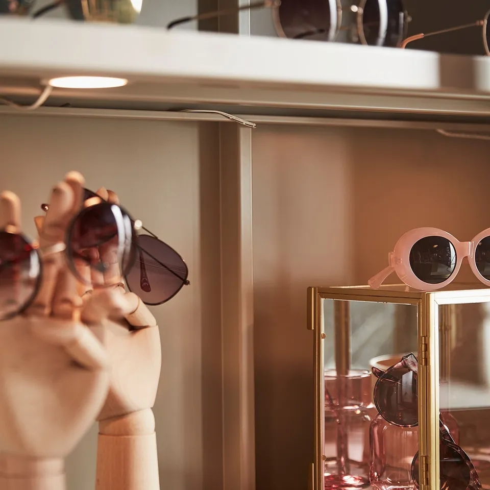 Display of stylish sunglasses on modern, minimalist mannequins and glass shelves, featuring various designs and colours.
