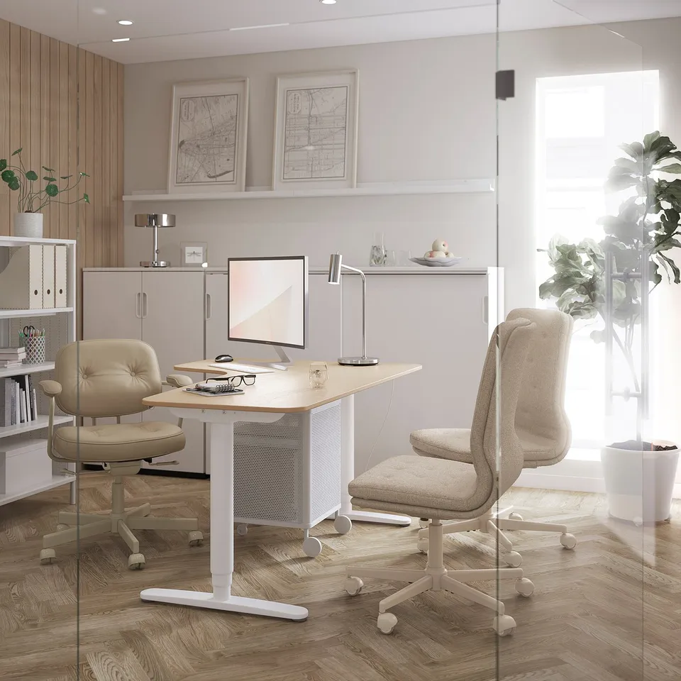 Modern home office with GALANT desk in light wood, chair, monitor, lamp, shelves, and maps.