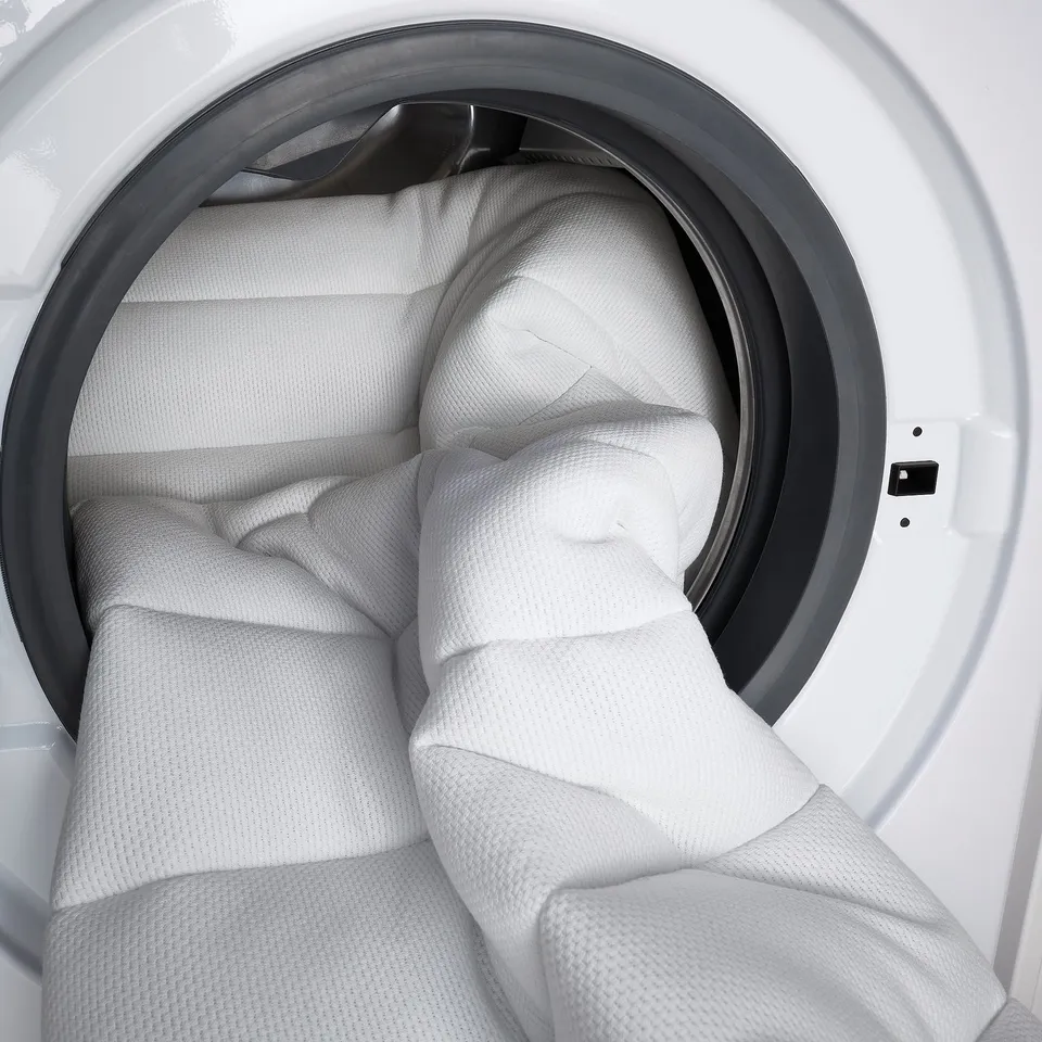 Image shows a white, thick, rolled firm foam mattress placed inside a dry machine, ready for a wash, with a quilted cover.