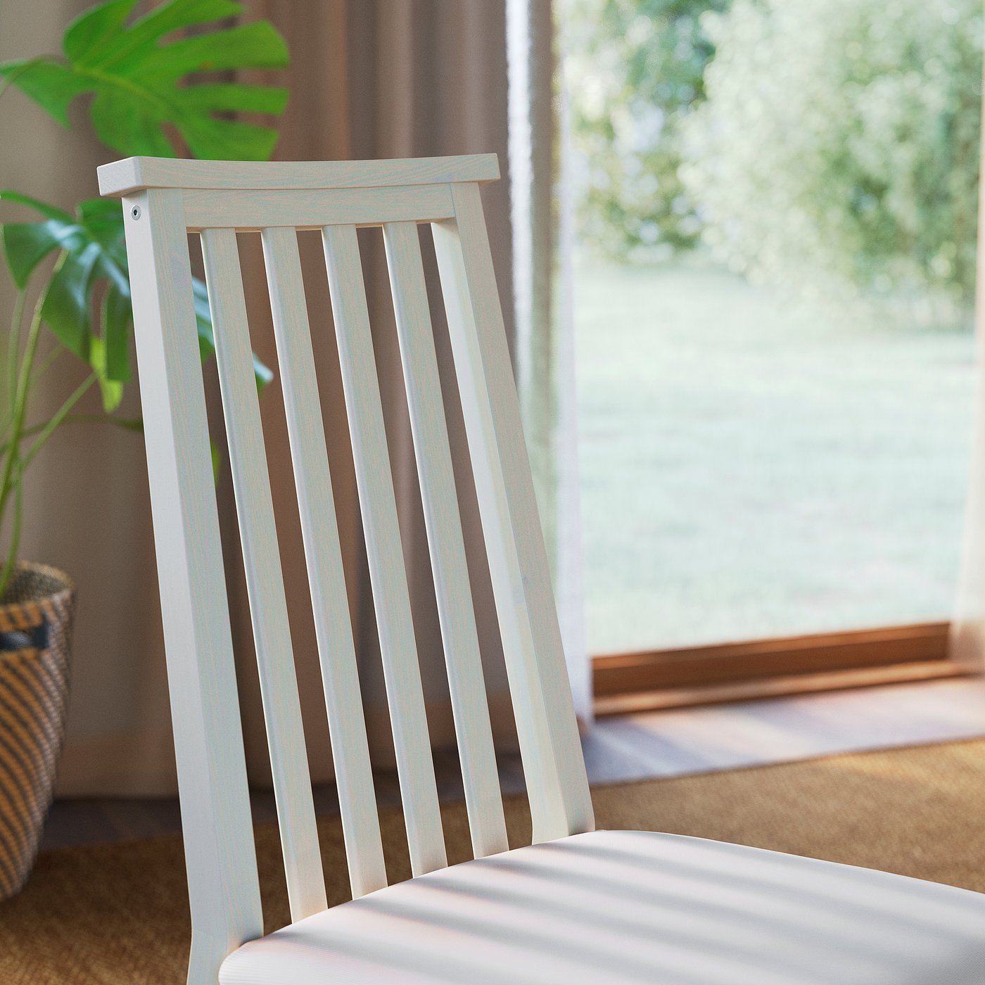 Modern white chair with slatted back and soft seat, near a window with greenery.