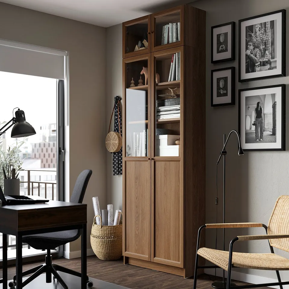 Modern home office with BILLY bookcase, desk, and city views. Includes lamps, wicker basket, chairs, and wall photos.