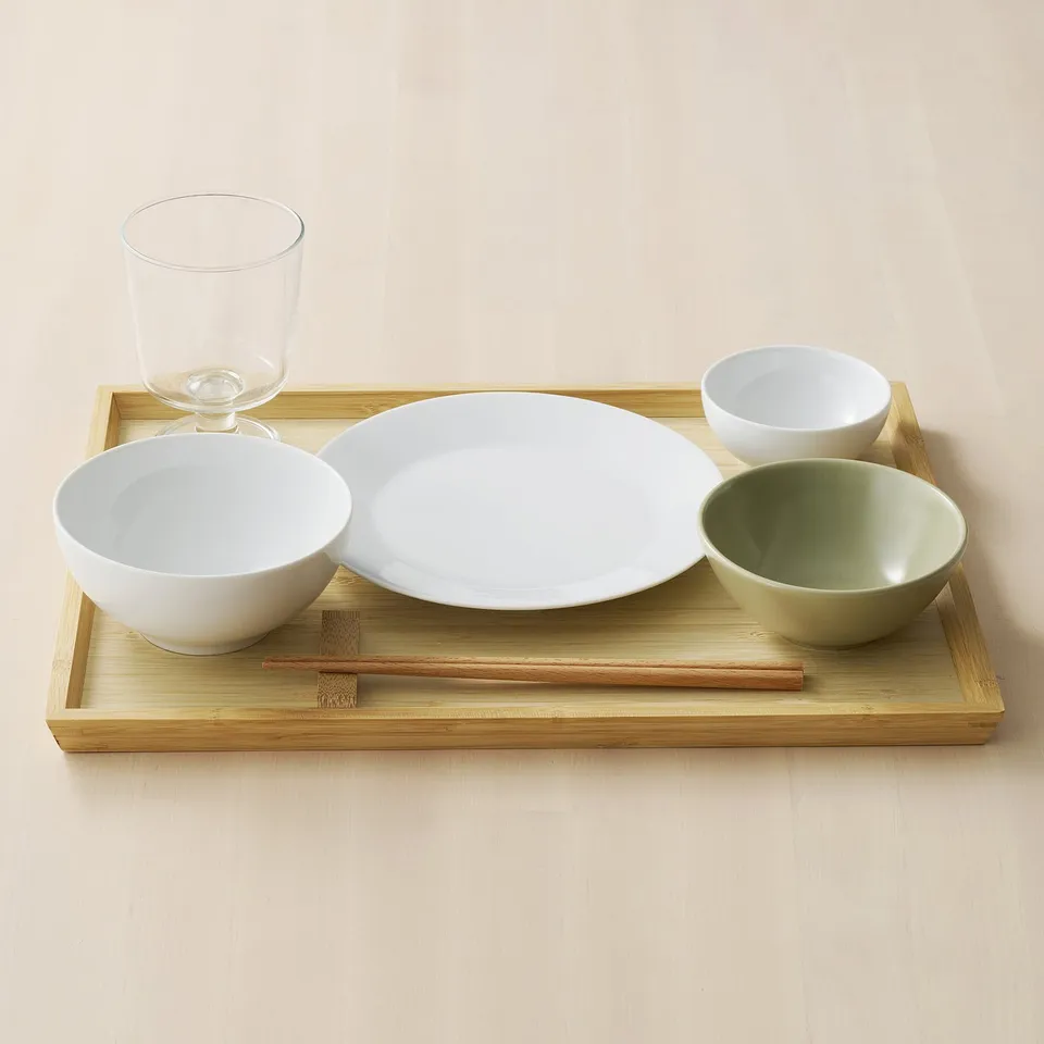 Bamboo tray with bowls, plate, glass, and chopsticks for dining.