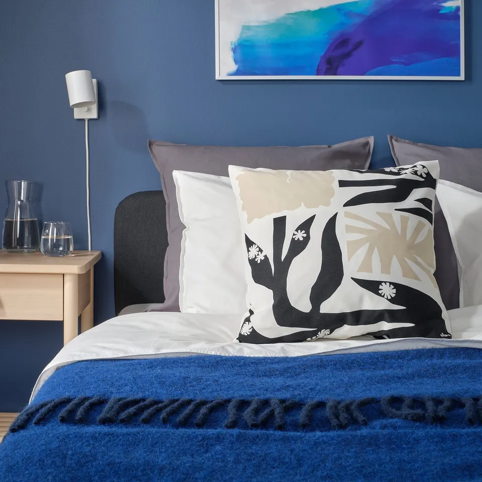 Blue bedroom with bed, DRABOR pillow, throw, and bedside table with lamp.