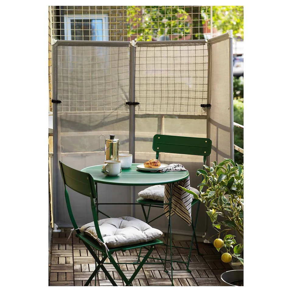 Small balcony setup with green YTTERSKÄR screen, table, and chairs, creating a cosy outdoor space.