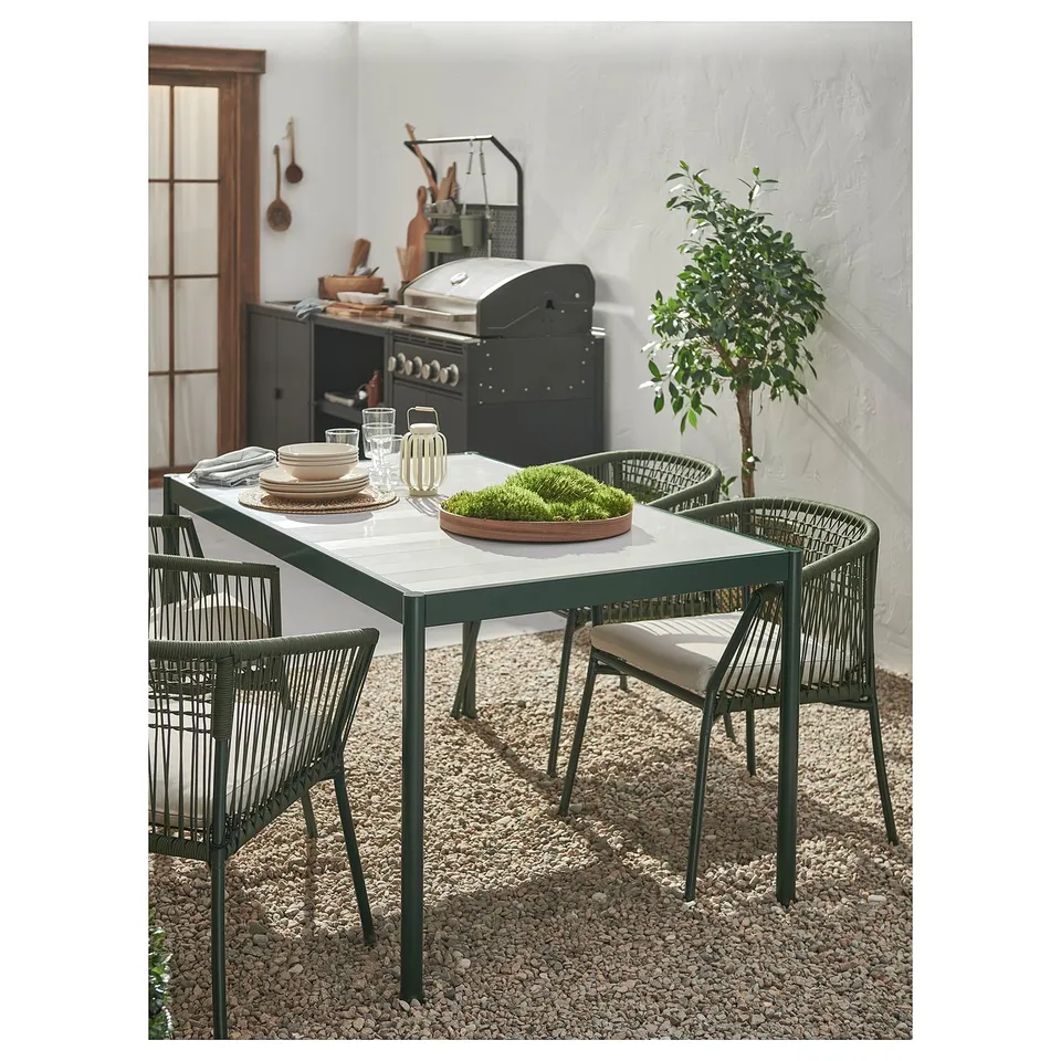 Modern outdoor dining setup with rectangular table, wicker chairs, plates, glasses, and grill.