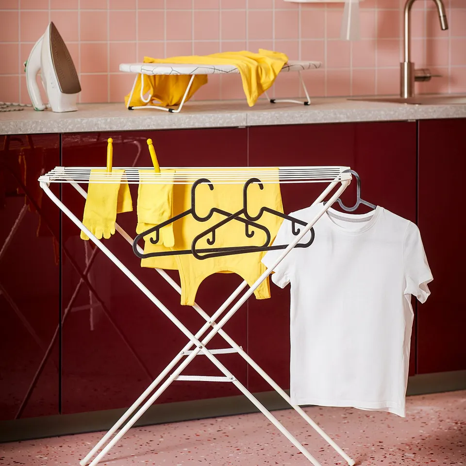 White JÄLL drying rack with yellow and white clothes. Modern, compact design with metal bars and plastic feet for stability.