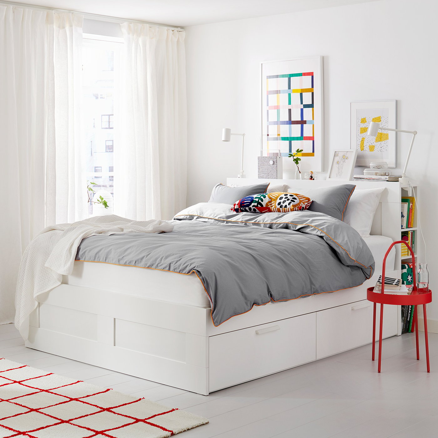 Modern white bedroom with BRIMNES bed, grey bedding, colourful pillows, side table, and vibrant rug.