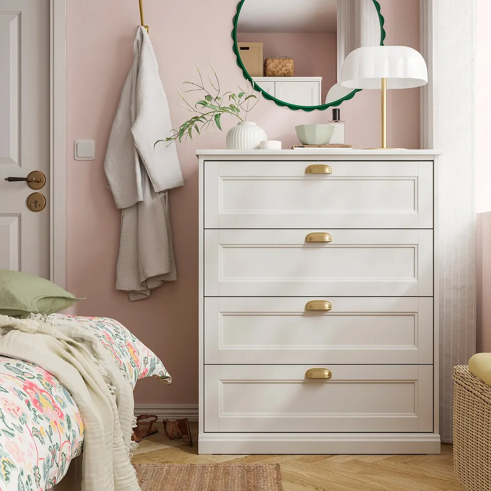 White chest with brass knobs beside bed, mirror, and lamp.