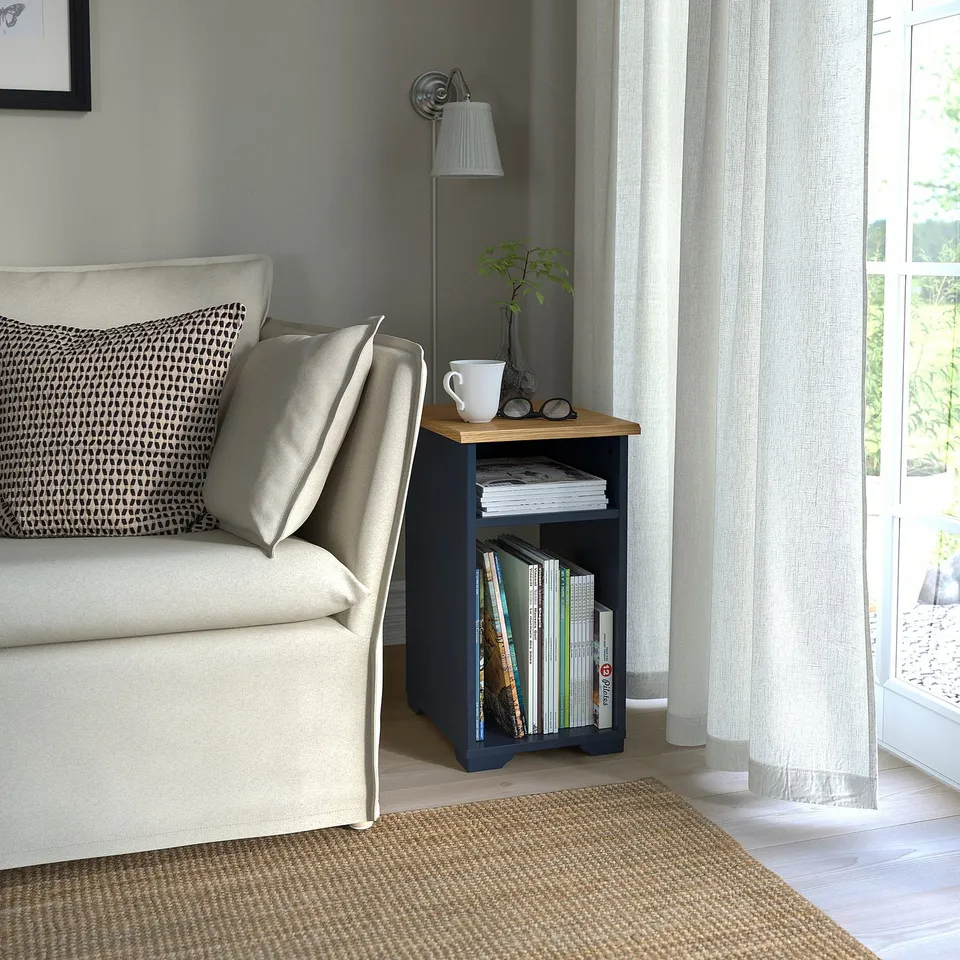 Navy SKRUVBY side table with books, mug & plant next to beige sofa.