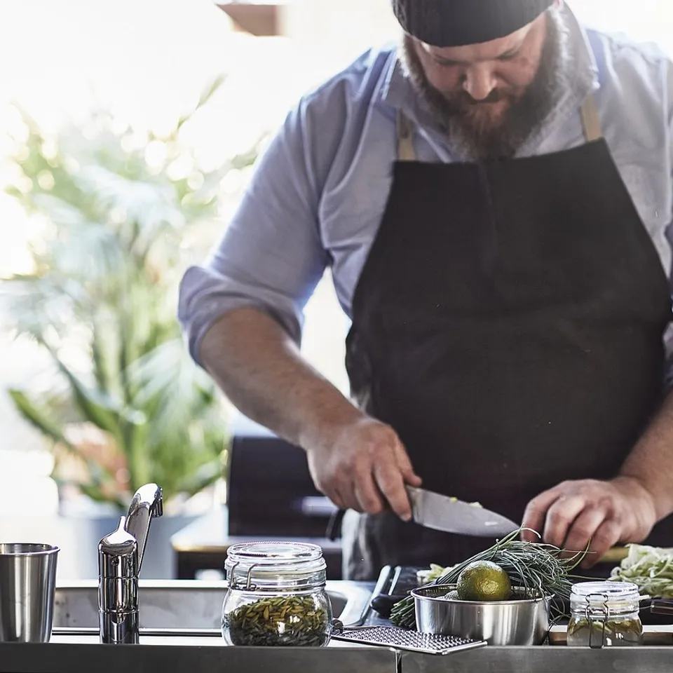 Person in black apron preparing food at kitchen island with various ingredients and utensils.