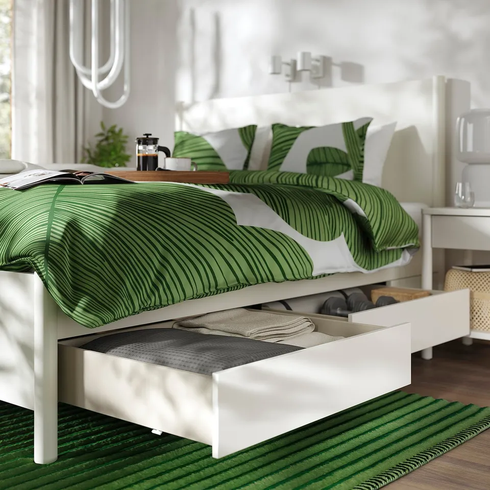 Bed with off-white frame, green bedding, and open underside drawers for storage.