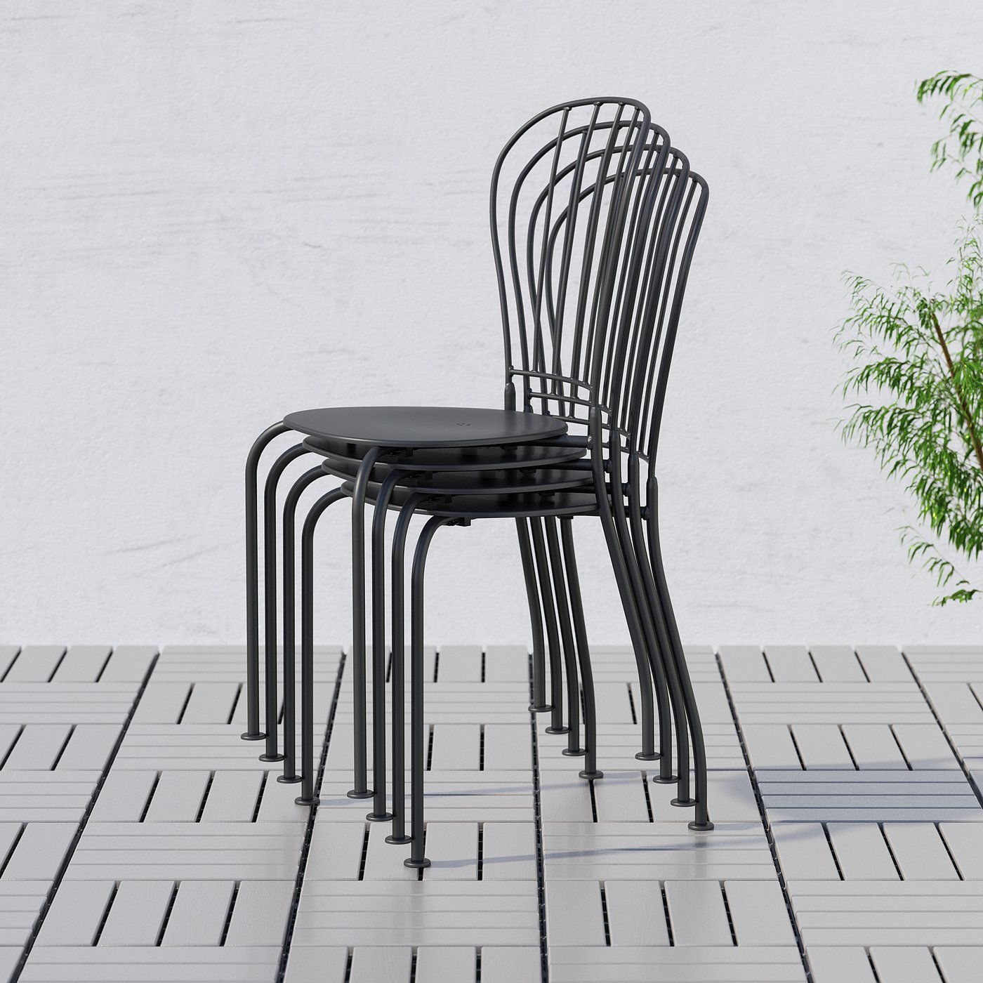 Three black metal chairs stacked outdoors, with intricate back designs, featuring drain holes for easy water drainage.