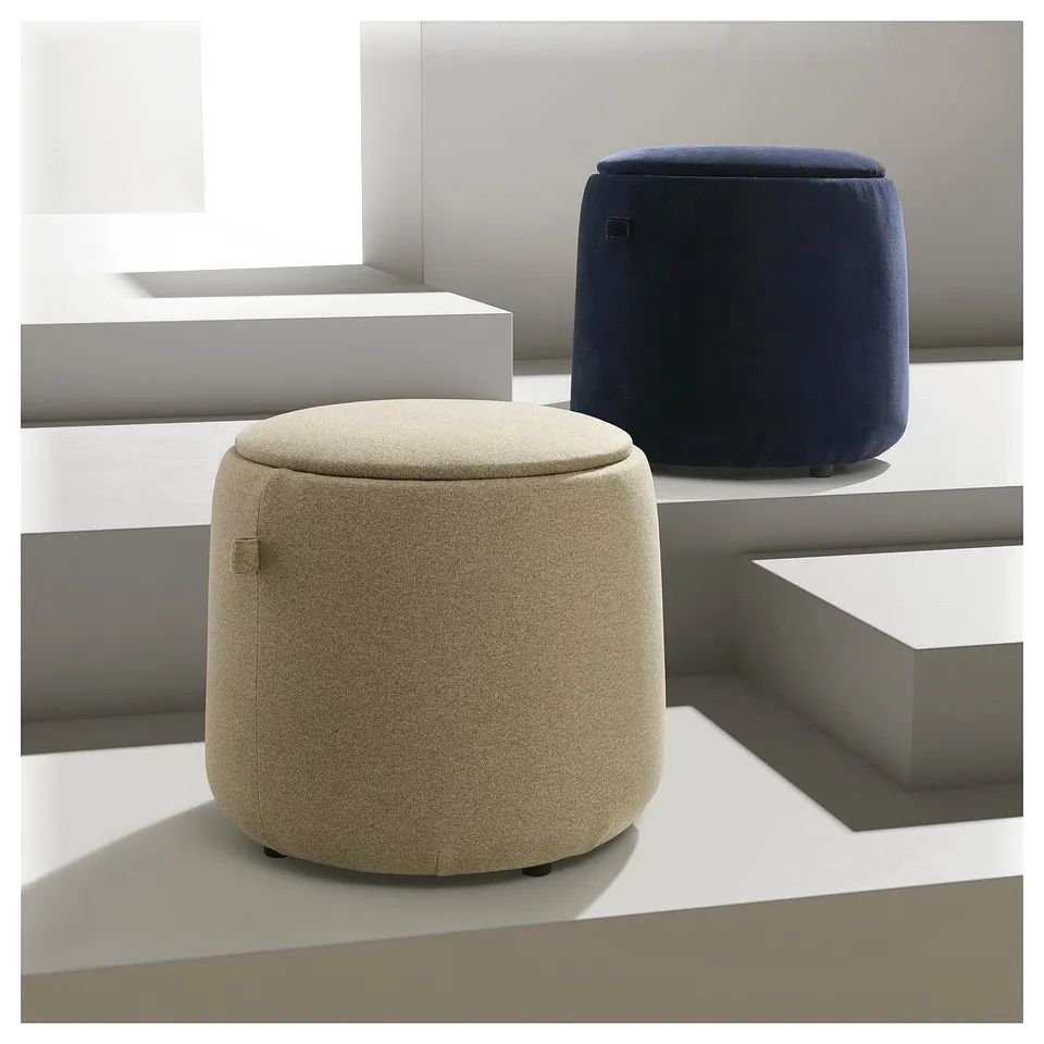 Two cylindrical stools, one beige and one dark blue, with rounded tops and hidden lid storage, set on white blocks.