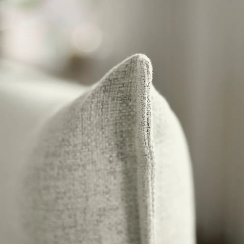 Close-up of upholstered sofa corner, showcasing soft, woven fabric texture and high-quality stitching detail.