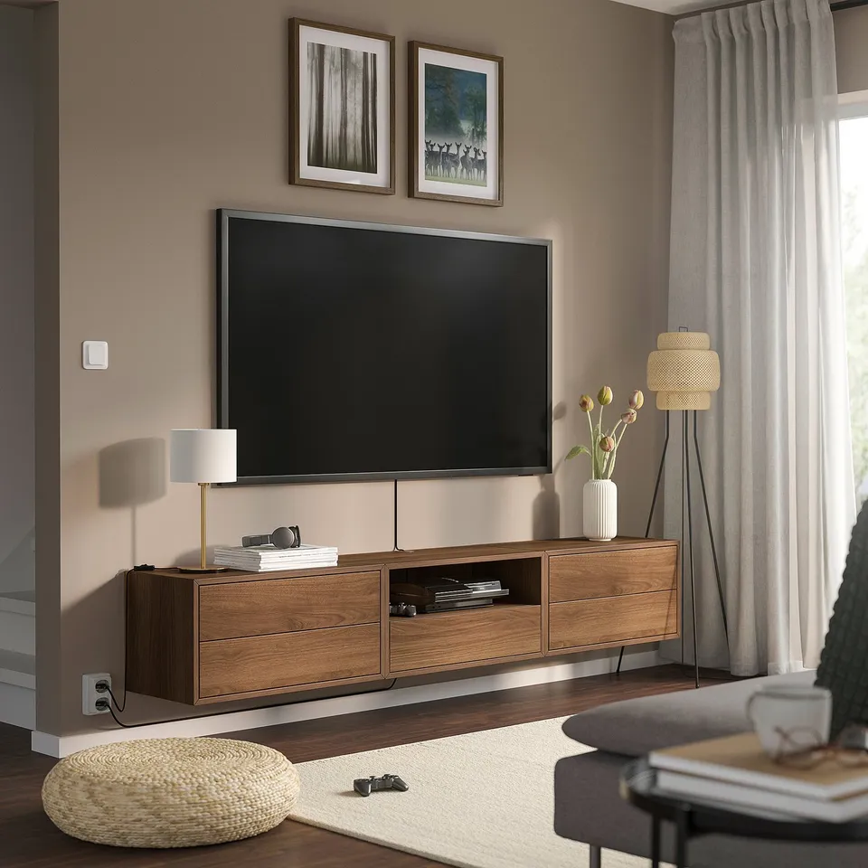 Modern living room with brown EKET tv unit, flat-screen tv, floor lamp, cream ottoman, and minimalist decor.