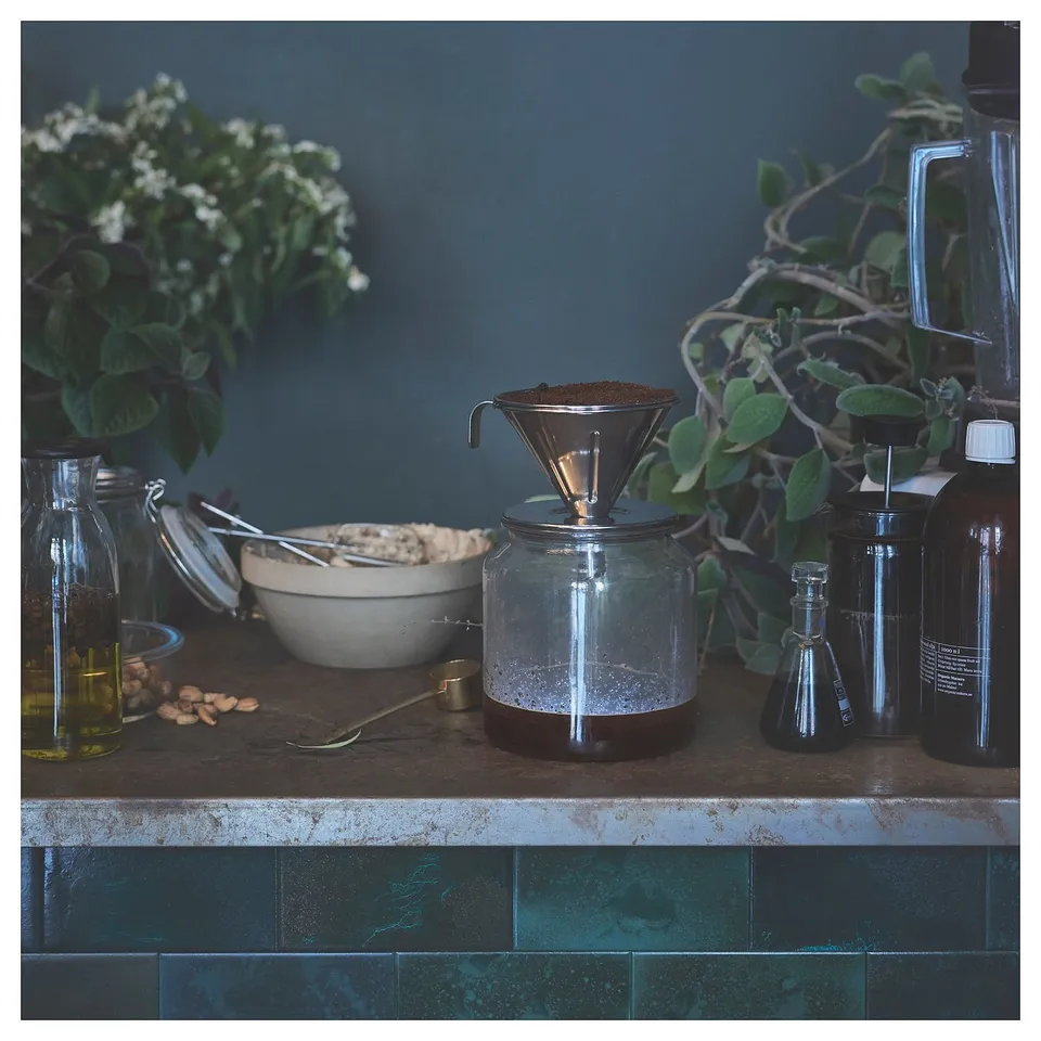 Stainless steel silver coffee philtre on counter with plants, jars, and bowls. Modern, minimalist kitchen decor.