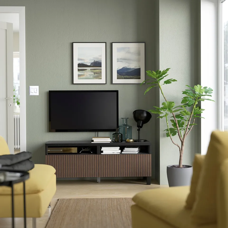 Modern living room with tv, yellow chairs, plant, and nature prints on sage green walls.
