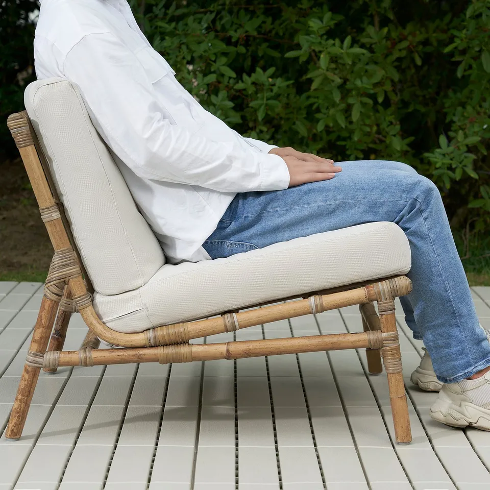 Person sitting on a rattan TVARÖ chair outdoors, with feet resting on the seat.
