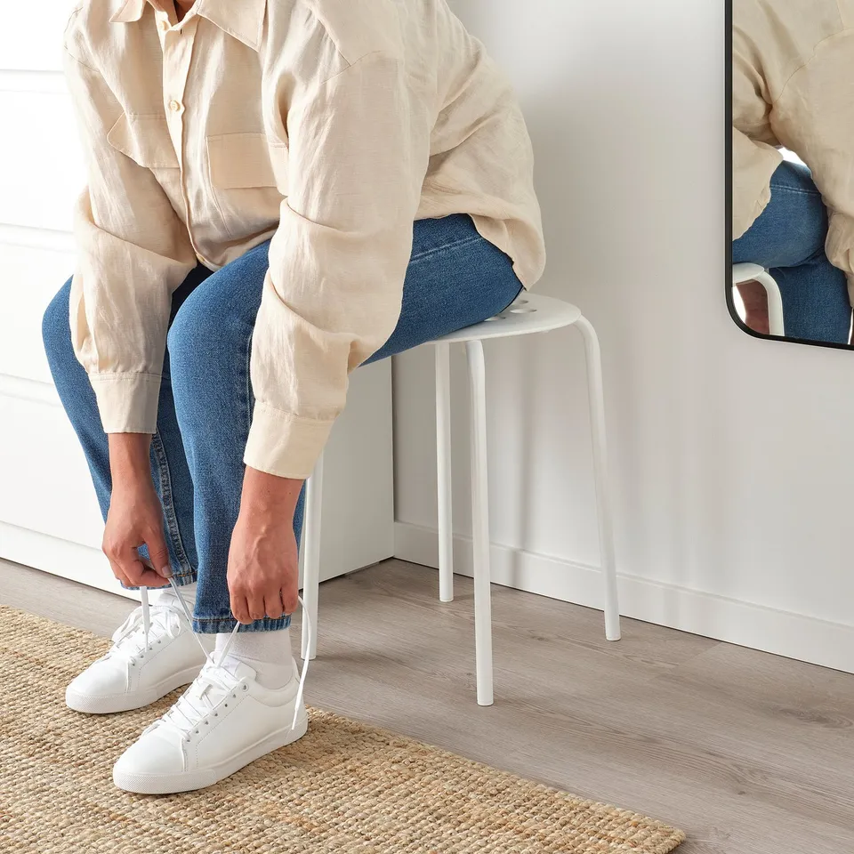 Person tying white trainers while sitting on white MARIUS stool.