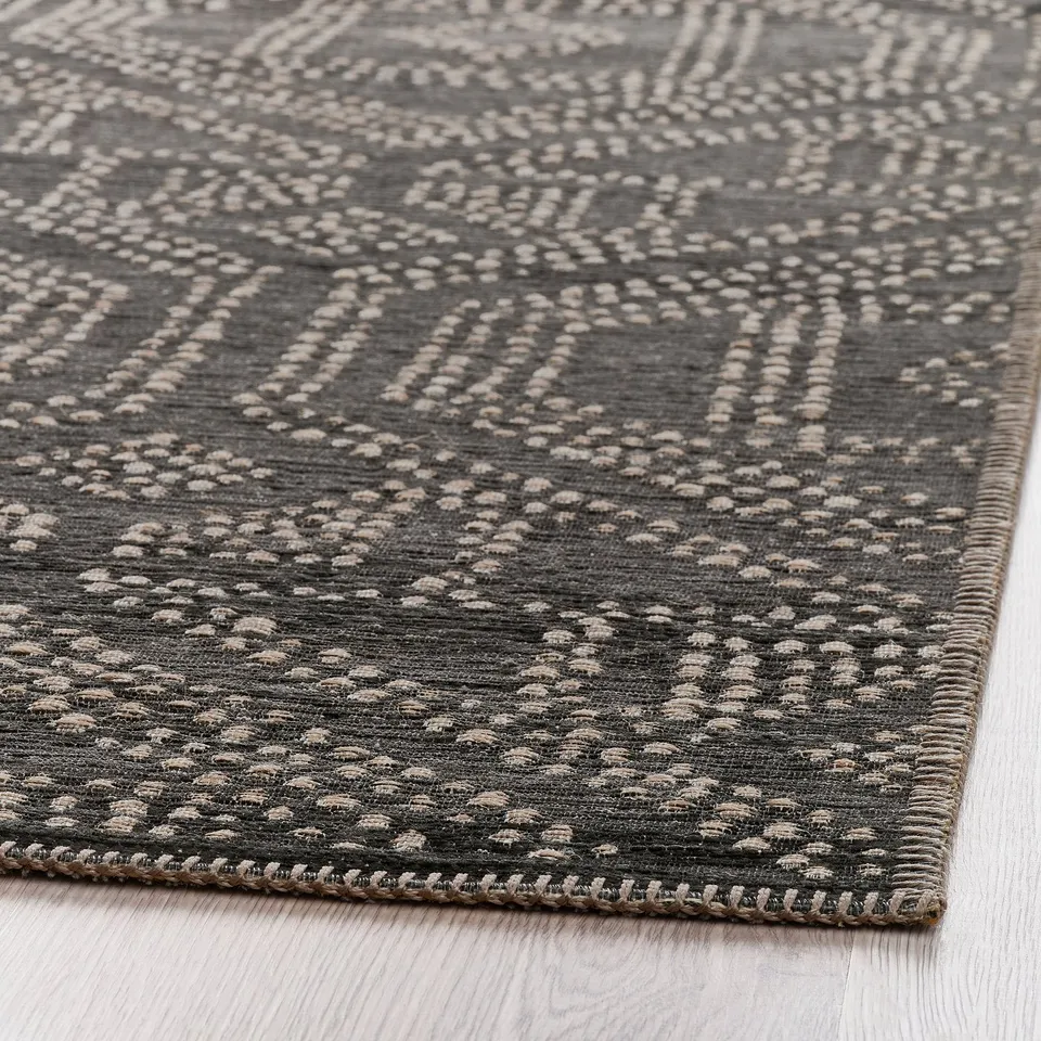 Textured rug with a diamond pattern in shades of grey on a wooden floor.