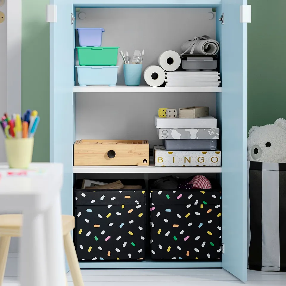 Light blue storage cabinet with shelves holding colourful boxes, office supplies, and games; designed for easy access by children.