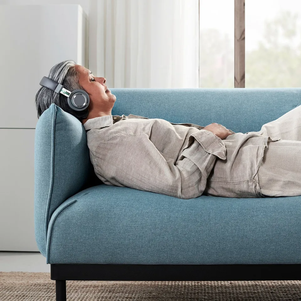 Person relaxes on blue ÄPPLARYD sofa, wearing headphones. Comfortable, modern design with soft fabric.