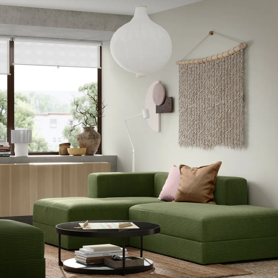 Modern living room with olive-green JÄTTEBO sofa, white pendant lamp, woven wall hanging, and wooden sideboard.