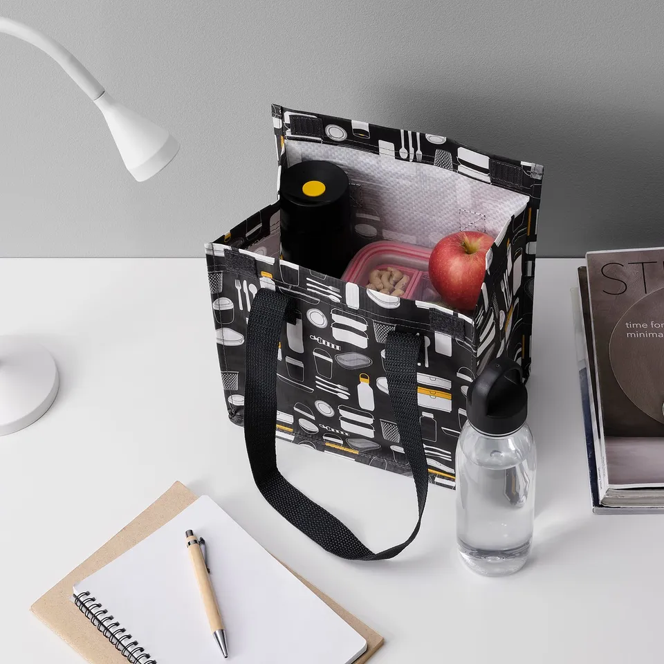 Lunch bag on desk with apple, water bottle, snack container, and notebook.