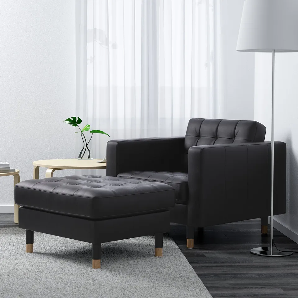 Modern living room with black armchair, ottoman, side table, floor lamp, and grey rug.