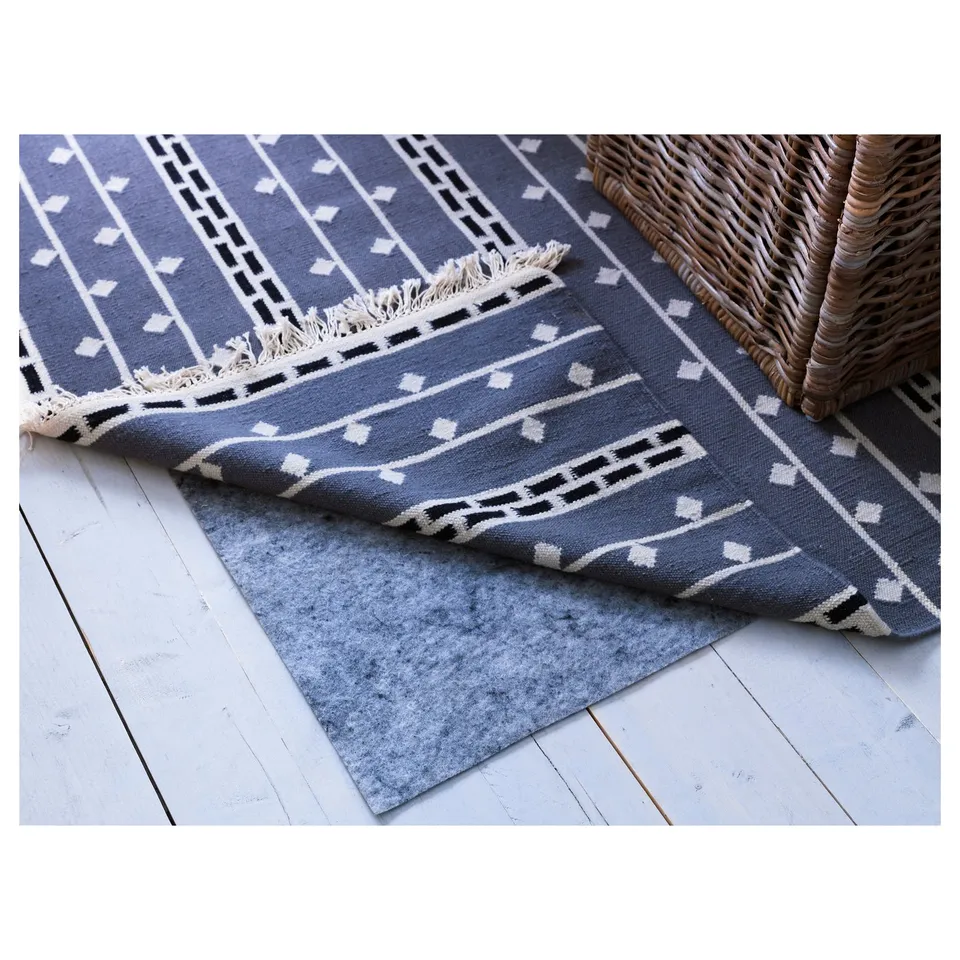 Two blue rugs with geometric patterns, one folded over a grey underlay on a light wooden floor, next to a woven basket.
