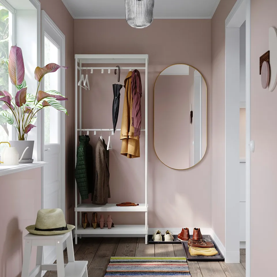 Entryway with pink walls, white MACKAPÄR coat rack and storage, large mirror, colourful rug, and potted plant near white door.
