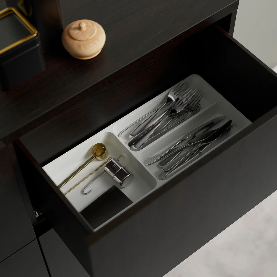 Open drawer of dark wooden desk, organised with cutlery and small items in compartmentalised tray.