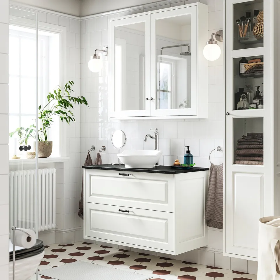 White bathroom vanity, black sink, mirrored cabinet, plant, tall cabinet.