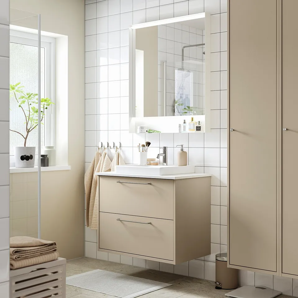 Modern beige bathroom vanity with drawer, white sink, mirror, and towels.
