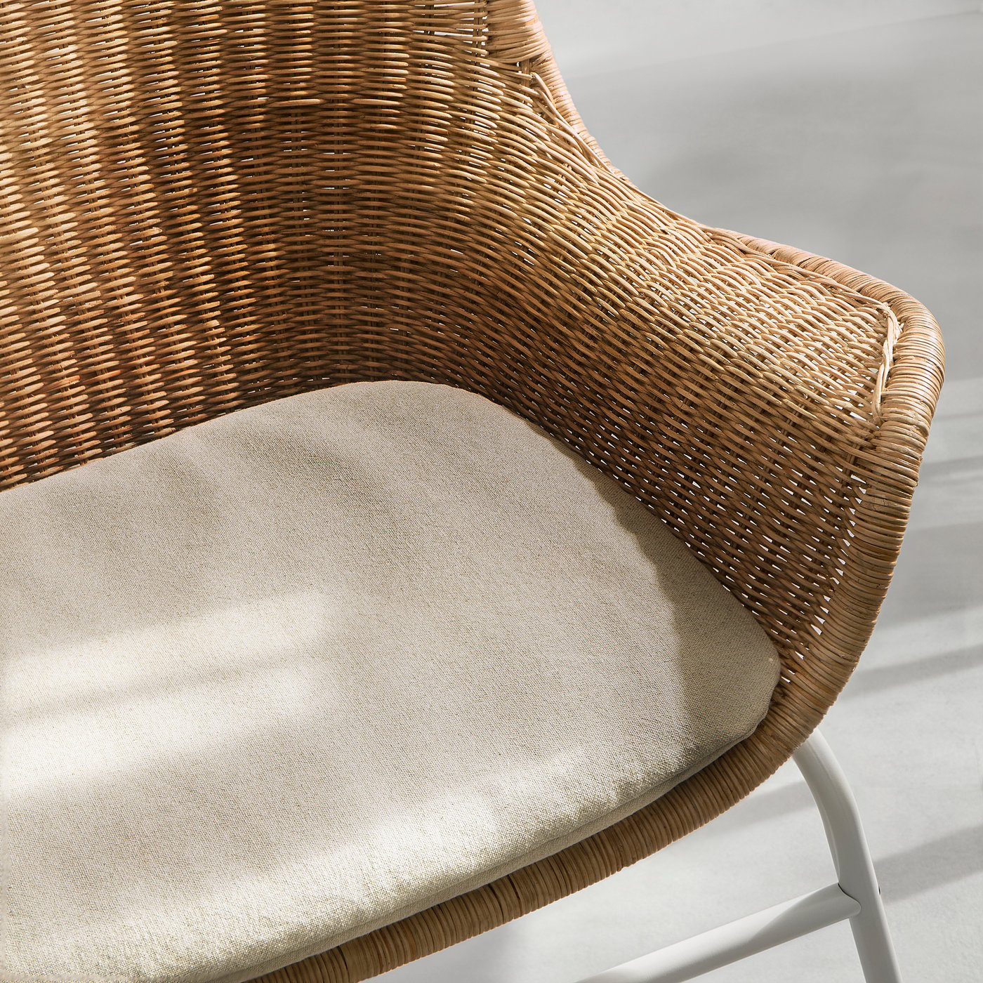 A wicker chair with a beige cushion, intricately woven, providing a cosy and stylish seating option.