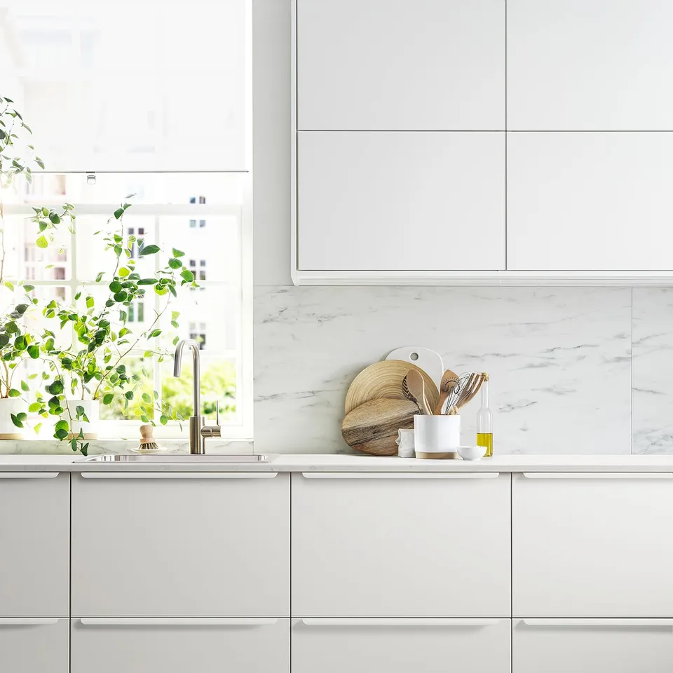 Modern white kitchen with marble backsplash and wooden utensils.