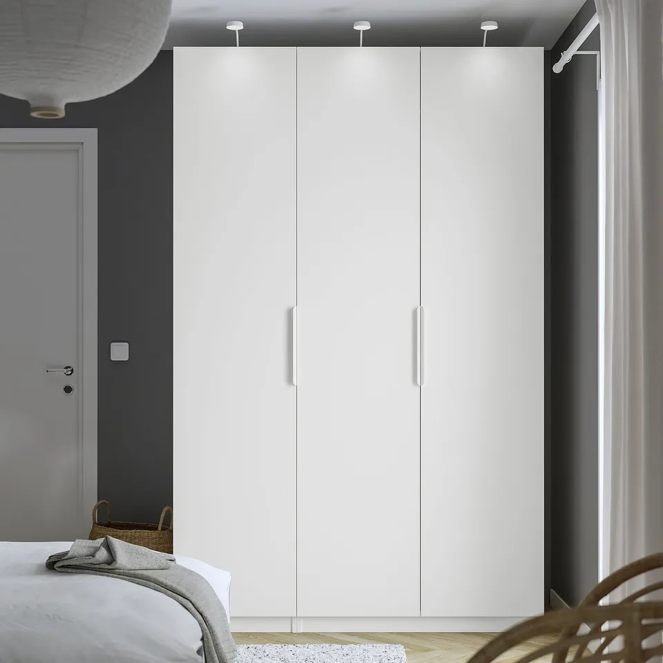 Modern bedroom with large white PAX wardrobe, tall and sleek, contrasting dark wall.,