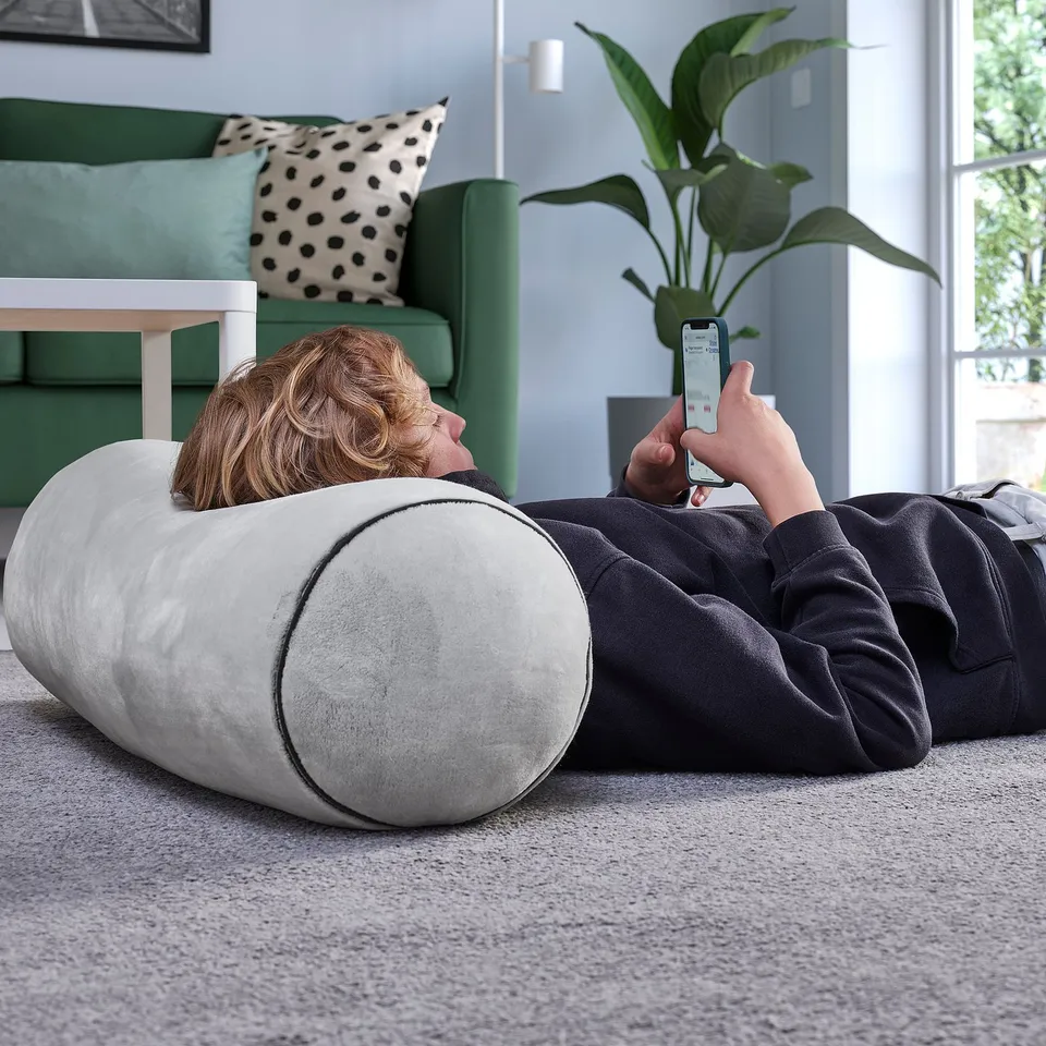 Person using smartphone on cylindrical cushion in cosy living room.