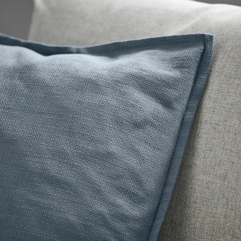 Blue-grey cushion cover with textured matte finish and zip, laid on a neutral surface.