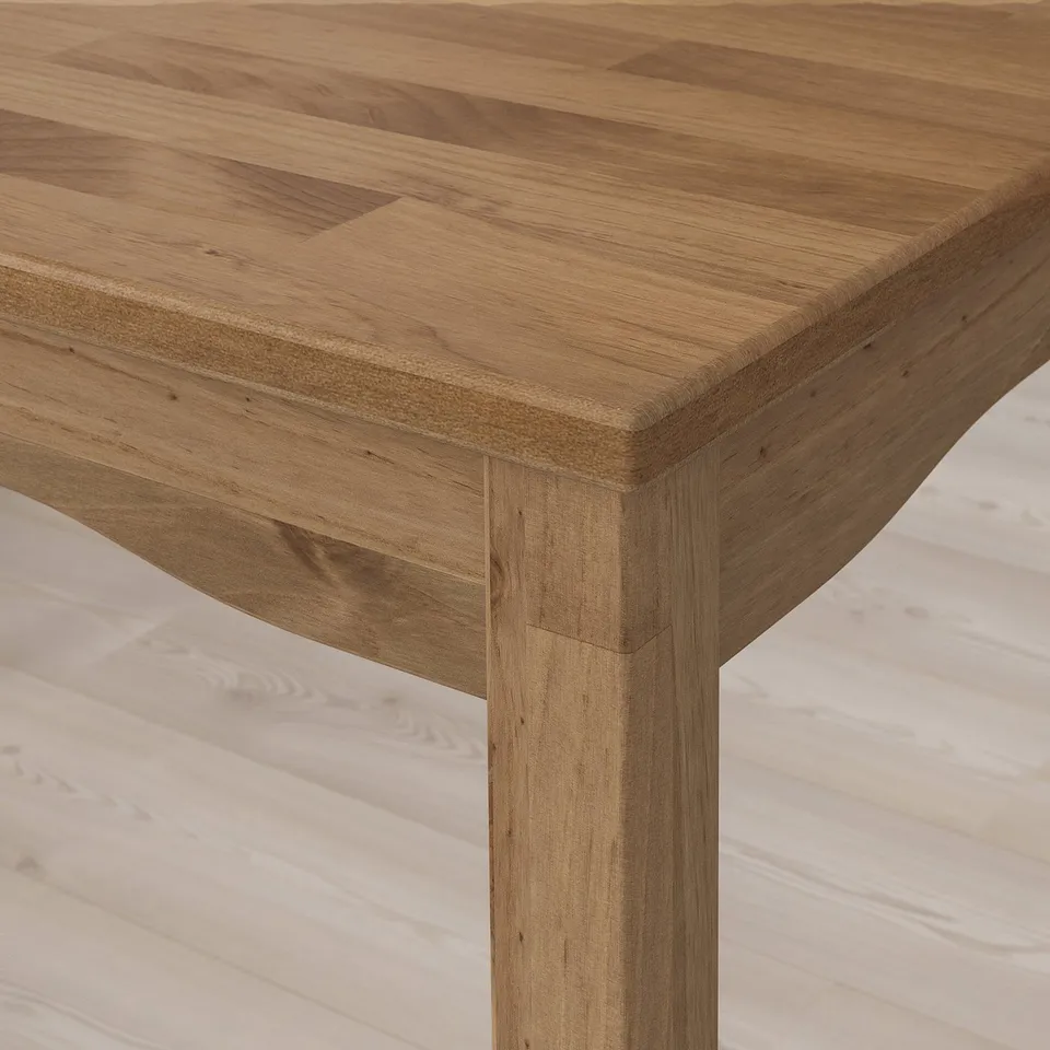 Close-up of a wooden tables edge, showcasing its polished, light brown surface and sturdy wooden leg with visible grain patterns.
